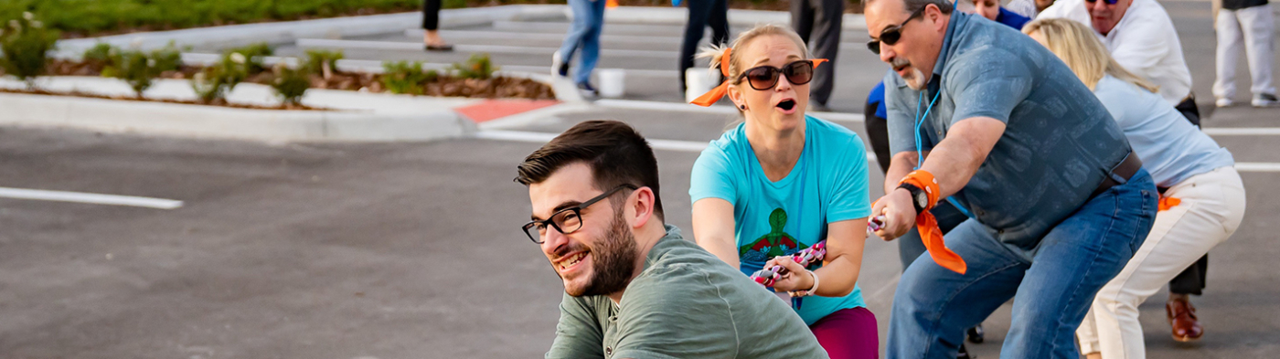 A diverse group of people playing tug-of-war in a parking lot